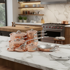 Mauviel M'Heritage M'150 S copper cookware set with 14 pieces, cast stainless steel handles, and curved lids displayed on a kitchen countertop.